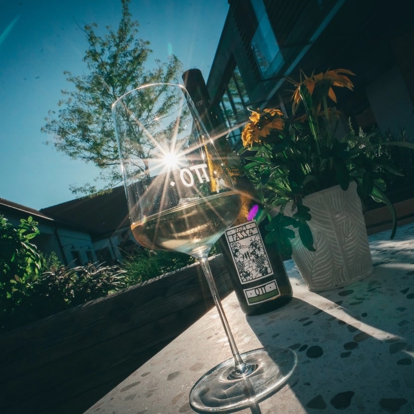 Fass 4 am Weingut Ott in der Sonne Ein Weinglas gefüllt mit 1/8 Fass 4 Wein vom Weingut Bernhard Ott steht auf einem Steintisch. Durch das Glas scheint ein Sonnenstrahl und die Reflektion der Sonne ist durch das Weinglas zu sehen.